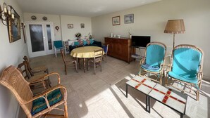 Un salon avec une table ronde, des chaises en osier, un canapé, un téléviseur et une lampe.