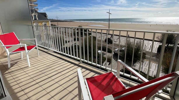 Un balcon avec vue sur la plage, une chaise rouge et une chaise blanche.