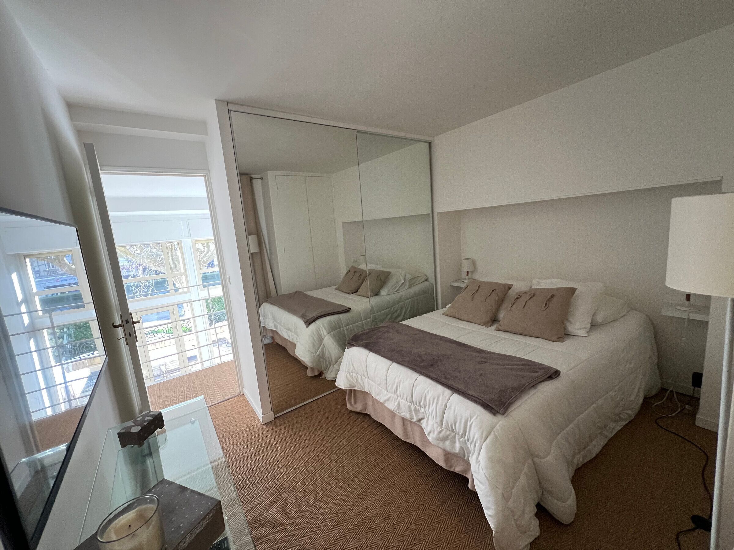 A hotel room with two beds, a large mirror, a glass table with a candle, and a view through a glass door.