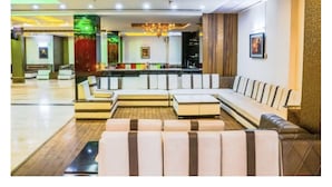 A modern lobby with a sectional sofa, a small coffee table, and a bar area in the background. - West Yard Hotels (New Delhi)