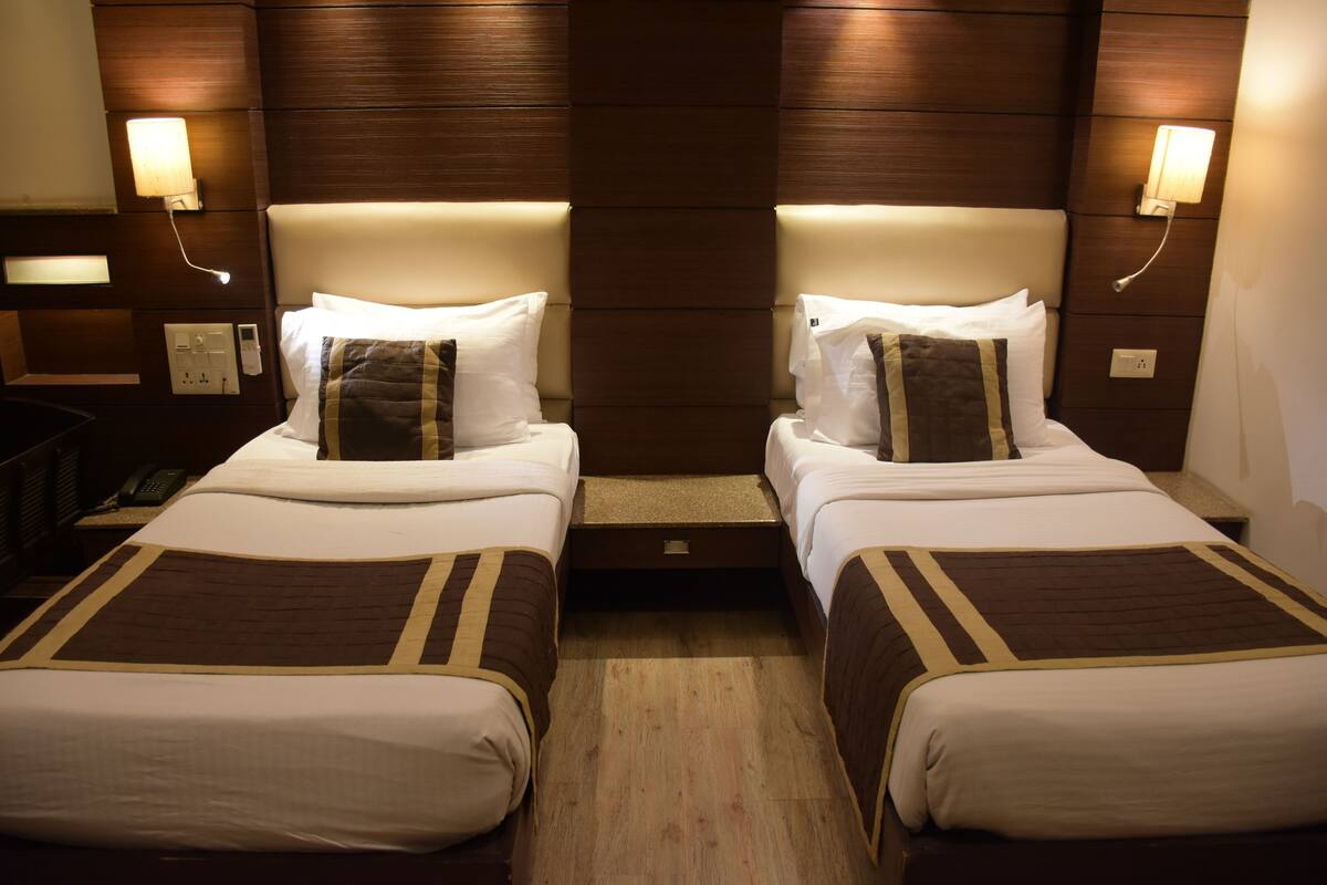 A hotel room with two beds, each with a headboard, bedside tables, and lamps.