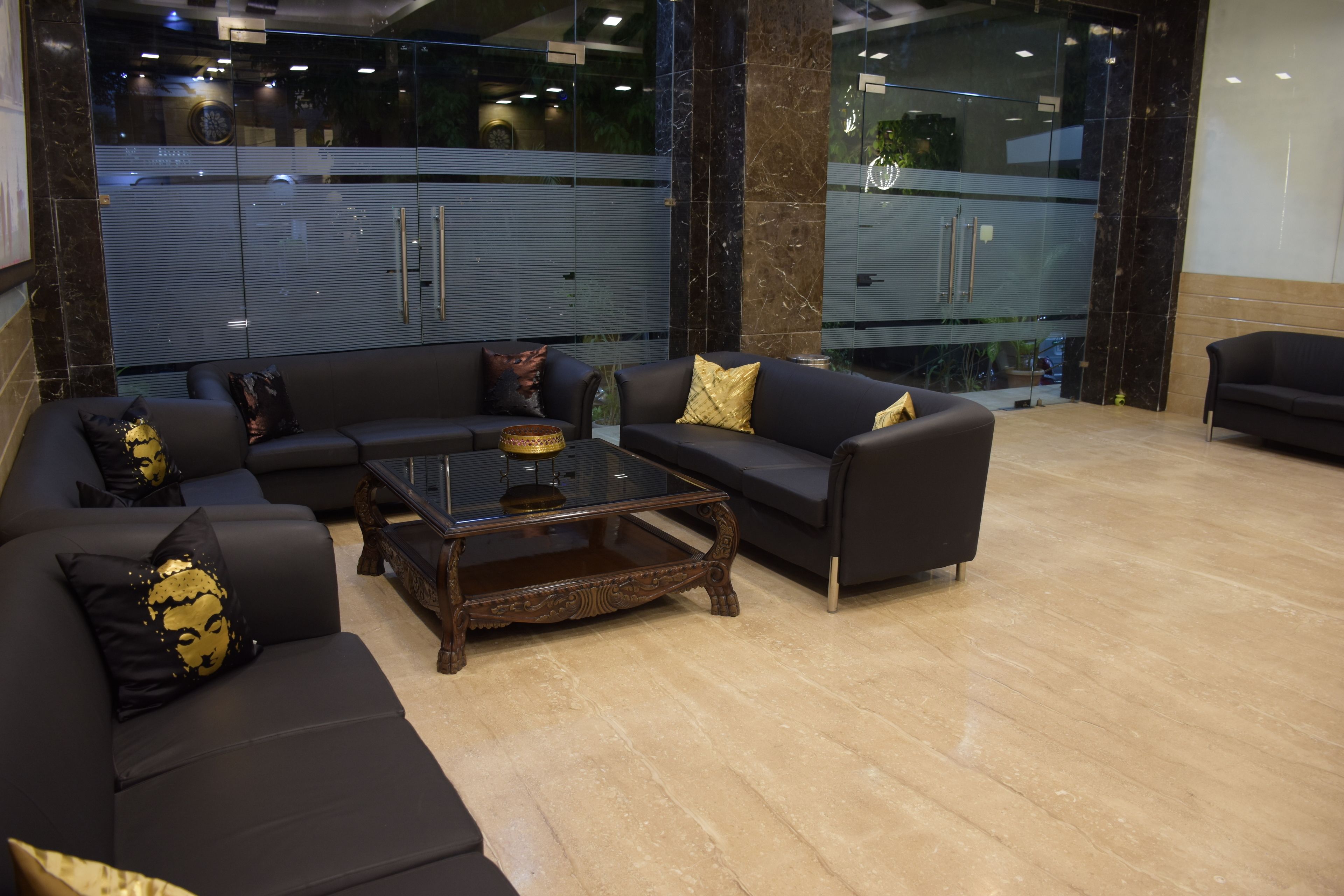 A modern lobby with black leather sofas, a wooden coffee table, and a glass partition.