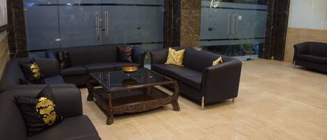 A modern lobby with black leather sofas, a wooden coffee table, and a glass partition.