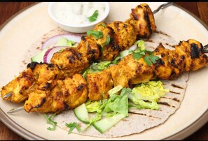 Grillade kycklingspett serveras på en tallrik med en klick vit sås och färska grönsaker som tillbehör.