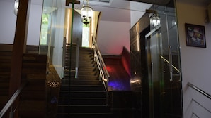 A staircase with glass railings, a red carpet, and a chandelier. - West Yard Hotels (New Delhi)