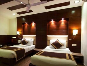 A hotel room with two beds, a ceiling fan, and wall-mounted lighting. - West Yard Hotels (New Delhi)