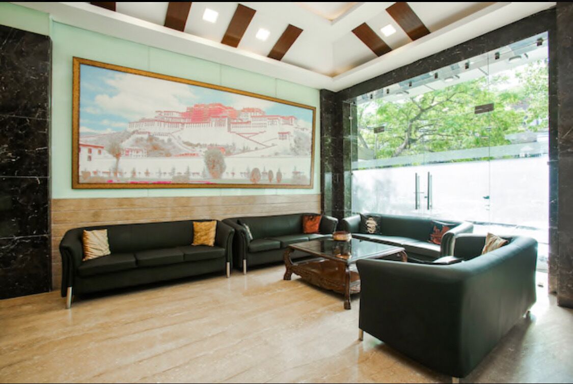 Een moderne lobby met een groot muurschilderij, een zwarte leren bank, een bijzettafeltje en een glazen scheidingswand.