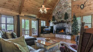 A cozy cabin interior with a stone fireplace, leather furniture, and a television.