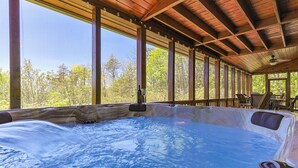 A hot tub with a wooden deck and large windows overlooking a forest.