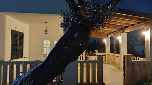 Un espacio al aire libre cubierto con una pérgola de madera, una cerca blanca y un árbol.