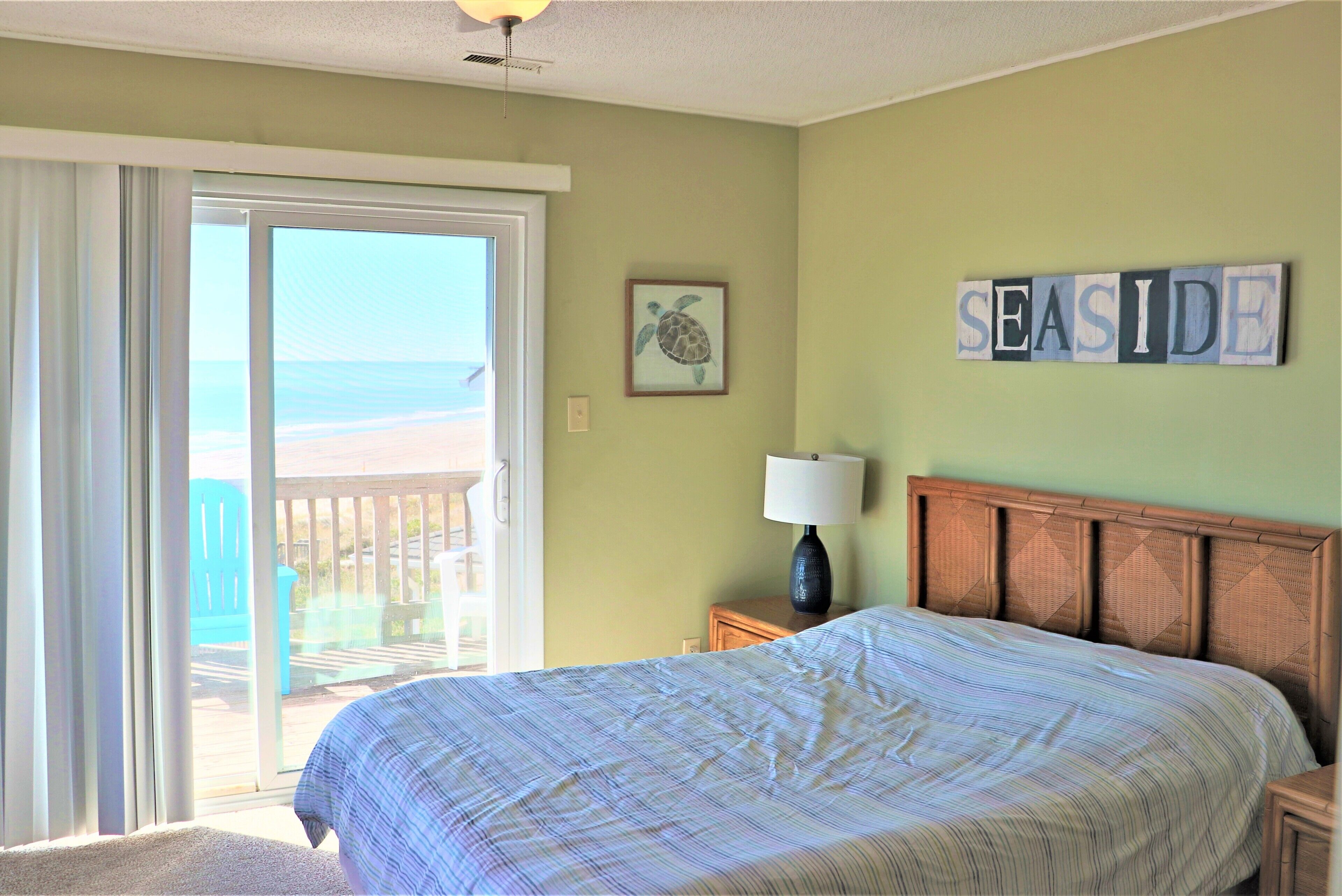 A bedroom with a bed, a nightstand, a lamp, a framed turtle picture, and a 'SEASIDE' sign on the wall.