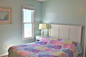 Quarto com cama, mesa de cabeceira, luminária, janela e radiador fixado na parede.