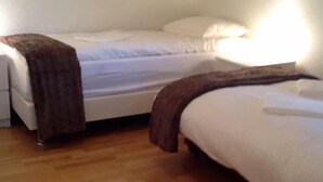 A bedroom with two beds, wooden flooring, and a nightstand with a lamp. - Sólheimar (Husavik)