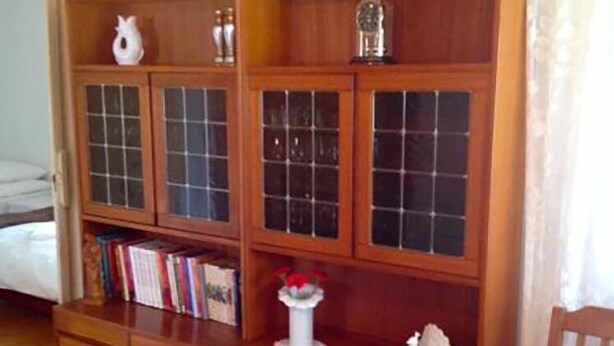 A wooden bookcase with glass doors, a white vase with red flowers, and a white ceramic sculpture. - Sólheimar (Husavik)