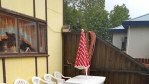 A wooden deck with white plastic chairs and a table, a red and white striped umbrella, and a wooden fence. - Sólheimar (Husavik)