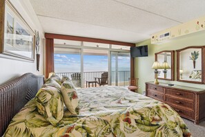 A hotel room with a large bed, a balcony with a view, a television, and a dresser.