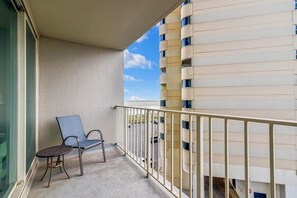 A balcony with a chair and a small table, overlooking a building with a view of the sea.
