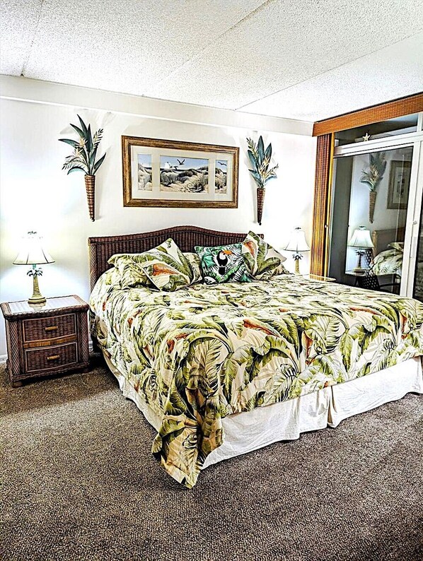 Une chambre à coucher comprenant un lit, deux tables de chevet, une fenêtre avec des rideaux et des œuvres d’art accrochées au mur.