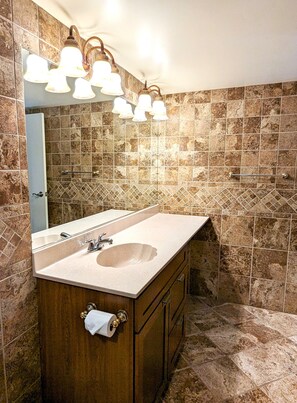 Une salle de bain avec un grand lavabo, un miroir et un luminaire placé au-dessus du miroir.