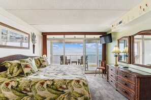 Quarto com cama, cômoda, televisão e varanda com cadeiras.