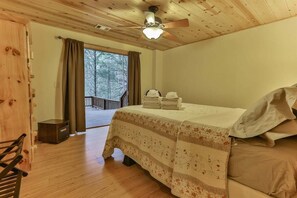 Ein Schlafzimmer in einer Holzhütte mit einem Bett, einem Deckenventilator und Blick ins Freie.