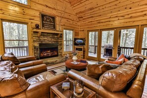 Ein Holzblockhaus-Interieur mit Ledersofas, einem Kamin und einem Kaminumrandung aus Stein.