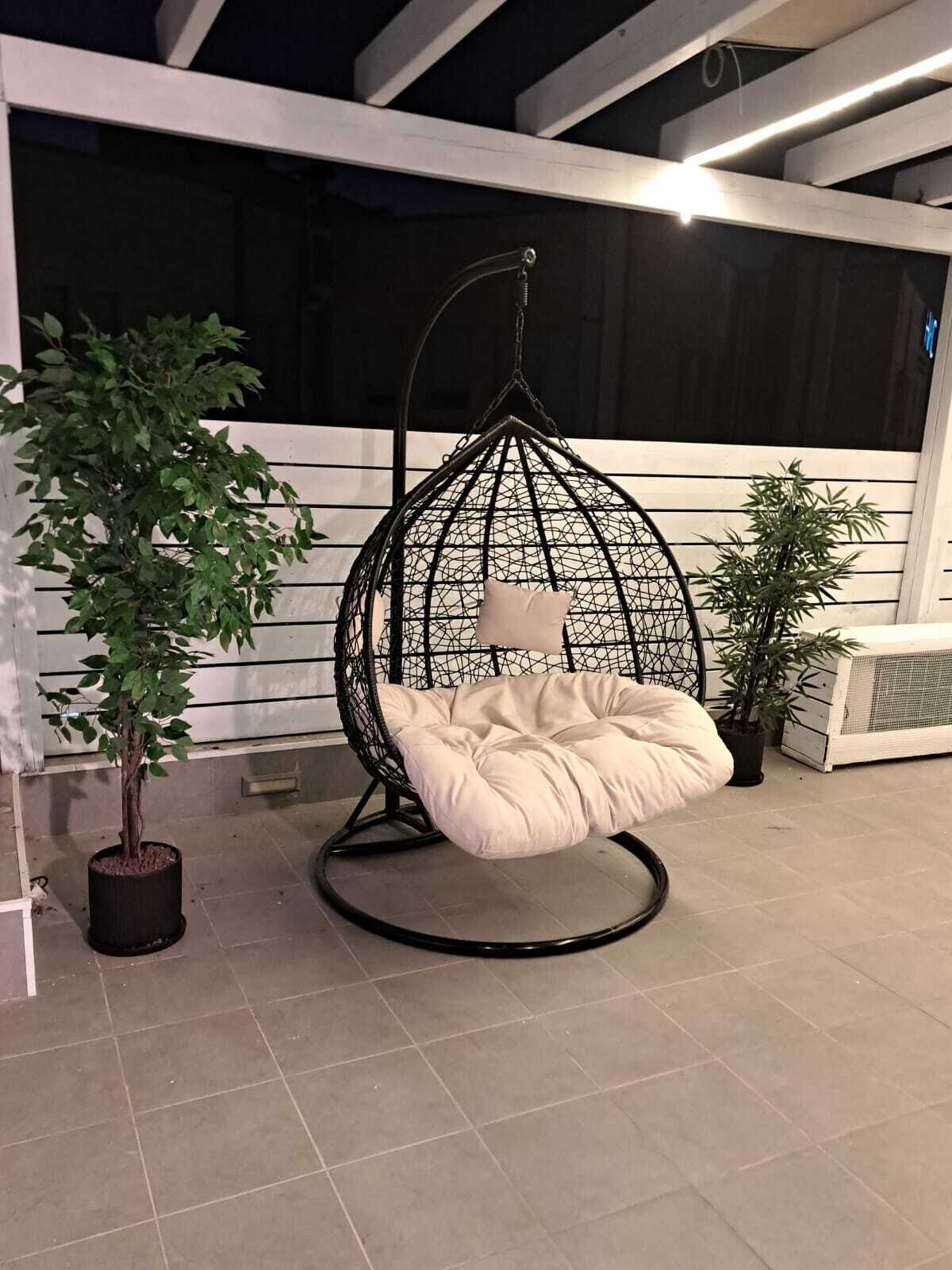 A hanging egg chair with a cushion, a potted plant, and a tiled floor.