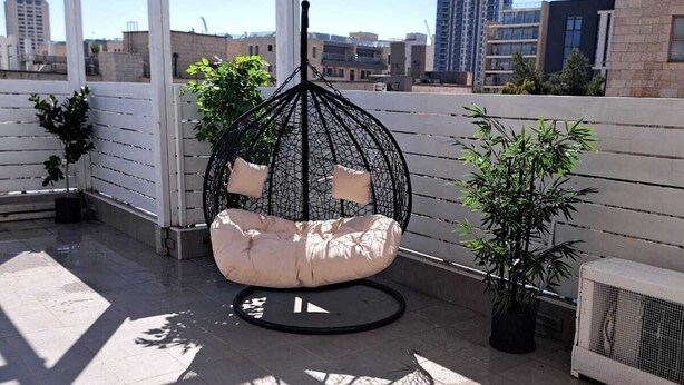 A rooftop patio with a hanging chair, potted plants, and a view of the cityscape.