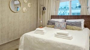 A hotel room with a wooden wall, a bed with white bedding, a round mirror, and a window with curtains.