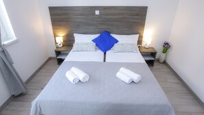 Un llit doble amb un edredó gris, dos almoines blanques i una almoina blava decorativa. Hi ha dues taules de nit amb làmpades, un ram d'un gerro i tovalloles damunt el llit.