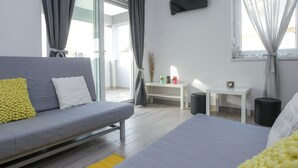Una habitació moderna amb un sofà gris, un llit, una taula petita i un televisor muntat a la paret.
