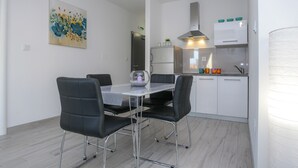 Una cuina moderna amb armaris blancs, una campana extractora d'acer inoxidable i una zona de menjador amb taula de vidre i cadires negres.