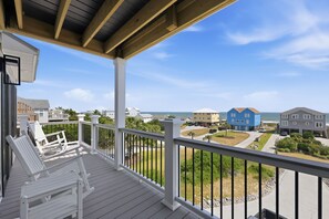 A wooden deck with white chairs, a view of a residential area, and a clear sky. - Ocean View Second-Row Duplex | Spacious 5BR | Beach Access Across Street (Emerald Isle)
