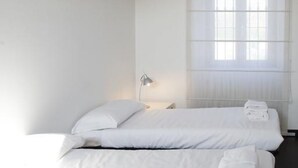 Ett hotellrum med två sängar, ett nattduksbord, en lampa och ett fönster med persienner.