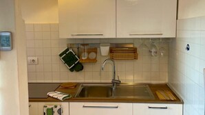 Une cuisine avec des armoires blanches, un évier en acier inoxydable et une horloge au mur.