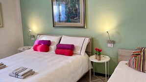Une chambre d’hôtel avec un lit, des oreillers, une table de chevet avec une lampe, un tableau encadré au mur et une petite table sur laquelle est posé un vase de fleurs.