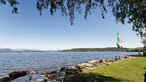 Une vue sur le lac, avec une table et des chaises, un mât avec des drapeaux, et une rive rocheuse.