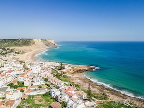 A coastal town with white buildings, a beach, and a rocky coastline.