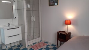 Kylpyhuoneessa on lasinen suihkuseinä, valkoinen pesuallas ja punainen lamppu puisen sivupöydän päällä.