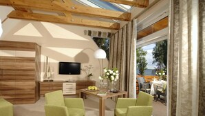 A modern living room with a wooden ceiling, a flat-screen TV, a dining table with chairs, and a view of the outdoors. - Aparthotel Am See (Plau am See)