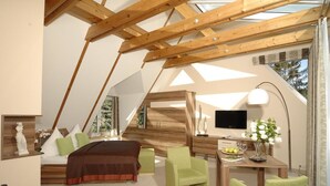 A bedroom with a sloped ceiling, wooden beams, a bed, a desk, and a TV. - Aparthotel Am See (Plau am See)