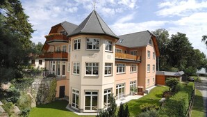 A multi-story house with a central tower, large windows, and a well-maintained garden. - Aparthotel Am See (Plau am See)