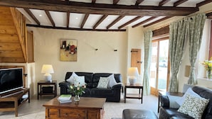 Ein gemütliches Wohnzimmer mit Holzboden, einem schwarzen Ledersofa, einem Couchtisch und einem Fernseher auf einem Holzständer.