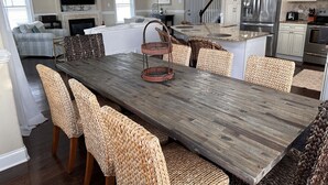 Un vaste espace de vie comprenant une grande table à manger en bois, des chaises en osier, une cheminée et une cuisine équipée d’appareils électroménagers modernes.
