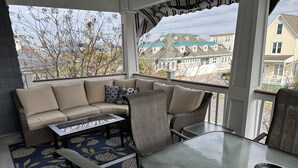 Un patio couvert avec un canapé, des fauteuils, une table en verre et un tapis à motifs.