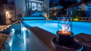 A swimming pool with a fire feature, a staircase leading to a covered area, and a building with a balcony. - Lovely apartment for 4 guests with pool, A/C, WIFI, TV, patio and panoramic view (Rijeka)