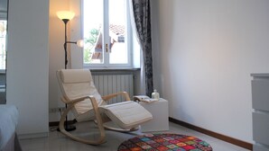 Une pièce avec un fauteuil à bascule, une petite table de chevet avec une lampe, une fenêtre avec des rideaux et un tapis coloré.