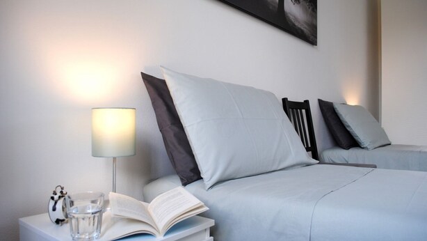 Une chambre à coucher bien rangée, avec un lit, une table de chevet sur laquelle se trouve une lampe, un livre et un verre d’eau.