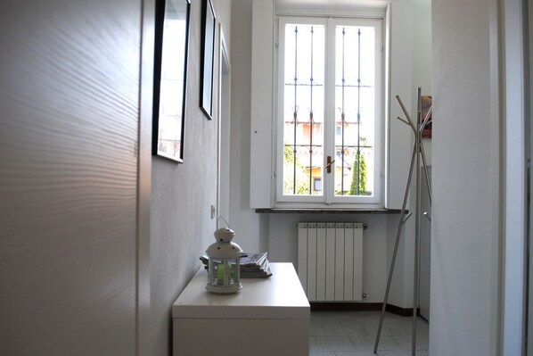 A narrow hallway with a radiator, a window with metal bars, and a white table with a lantern. - BNBOOK-CASCINA CRENNESE (GALLARATE)