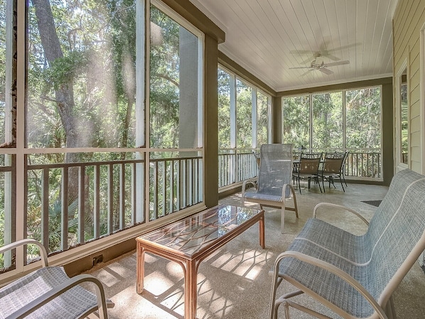 A covered porch with a glass table, two chairs, and a sofa.